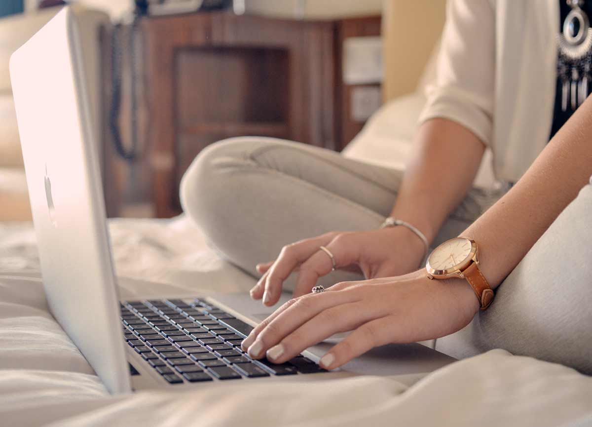 Woman typing on a computer while sitting on a bed