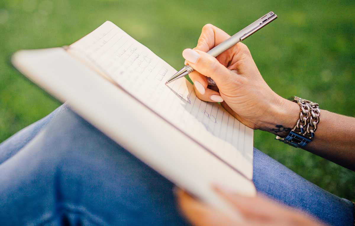 Hand with pen writing in a paper journal 