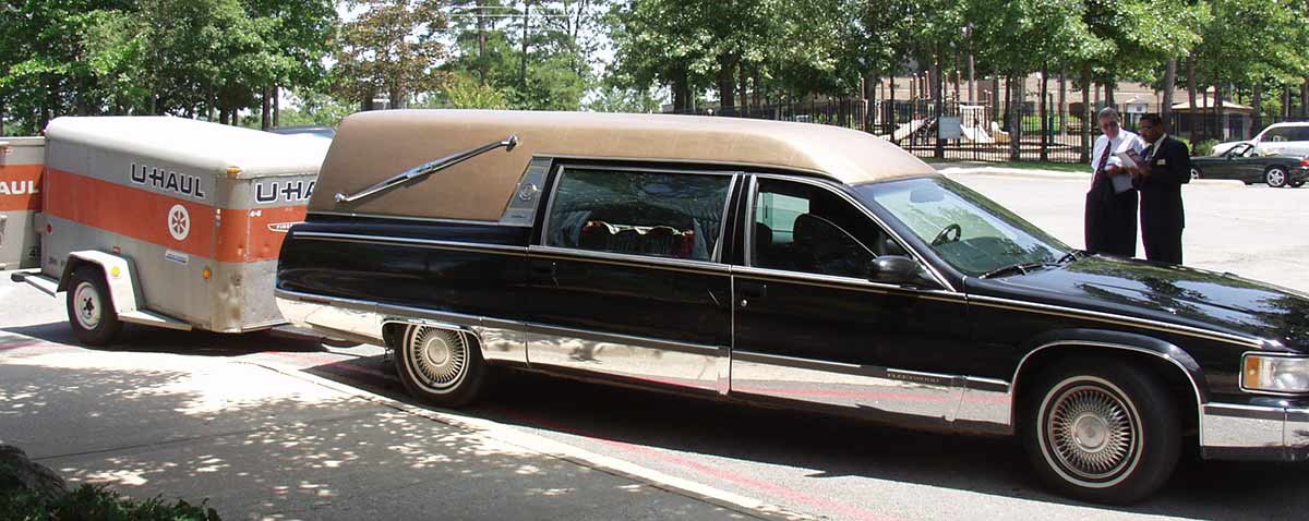 Hearse with a U-Haul trailer behind it at a funeral