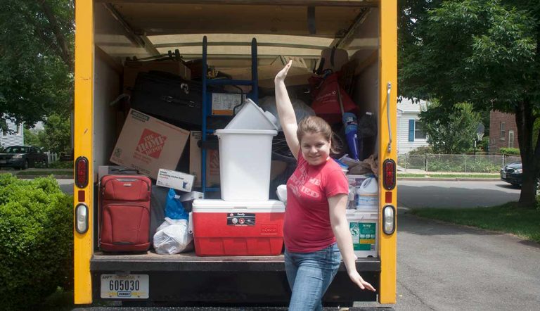 Open back of loaded moving truck, woman posing by it