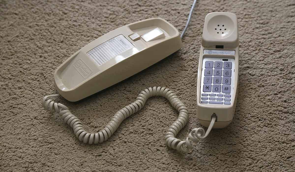trimline style phone on floor carpet, handset sitting next to phone base