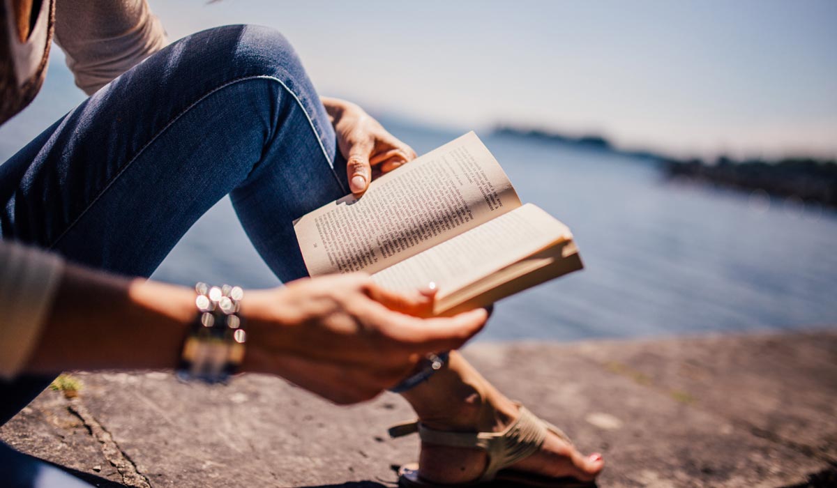 woman sitting by sea, reading a book