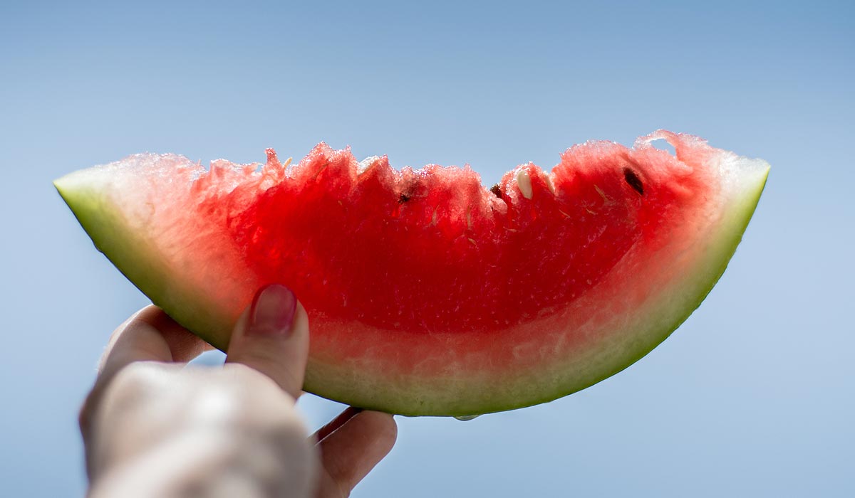 hand holding up a slice of watermelon against blue sky