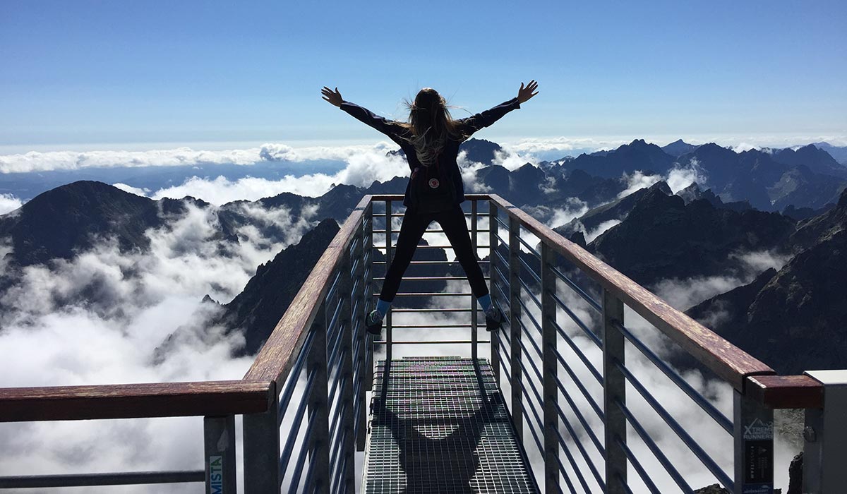 Woman with backpack and arms outstretched on observation platform high up in mountains