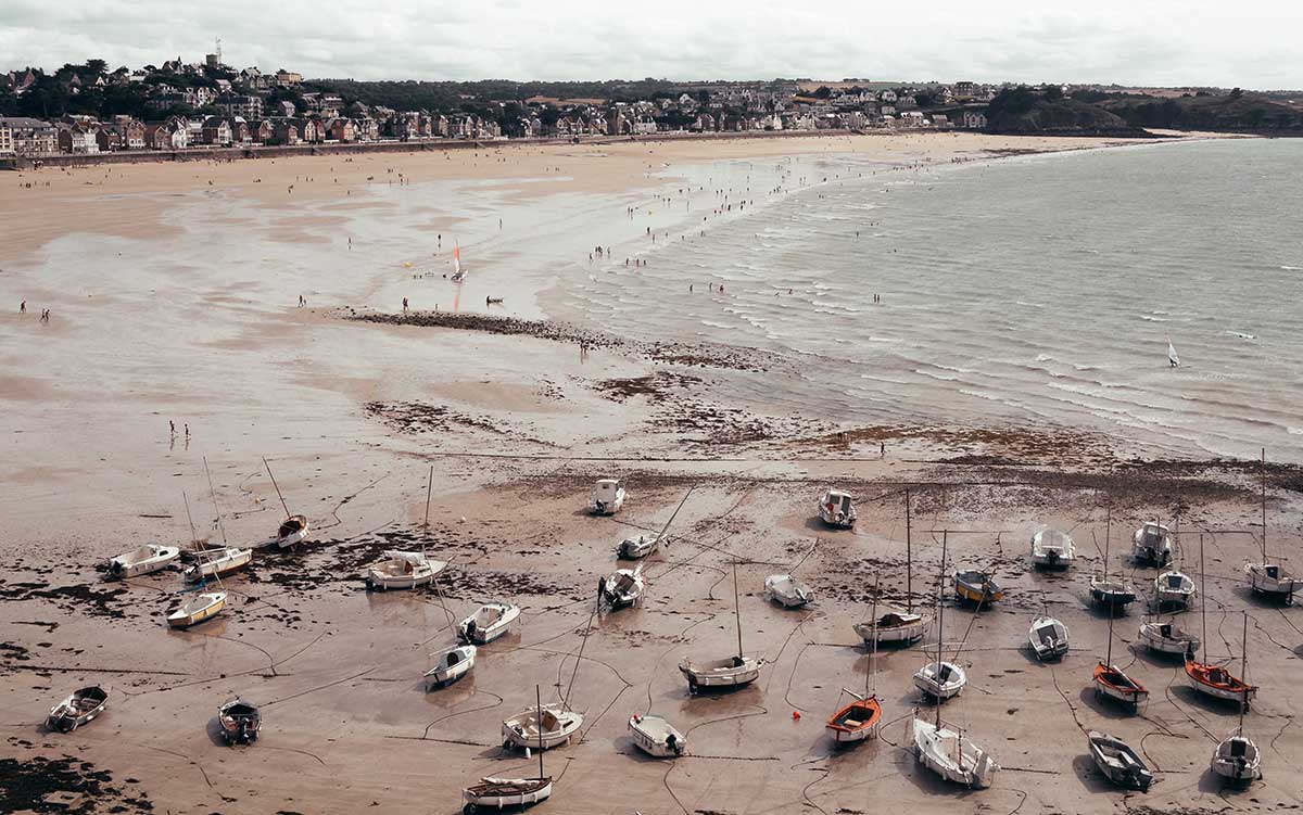 Harbor at low tide, boats sitting on bared seabed, people walking out to water's edge