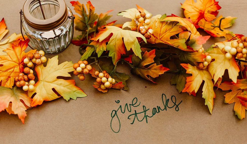 Leaves in fall colors, a candle, berries and the words "Give thanks" written on the table