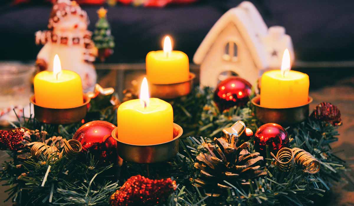 Arrangement of a group of lit candles, Christmas greenery, a miniature house and a snowman figure