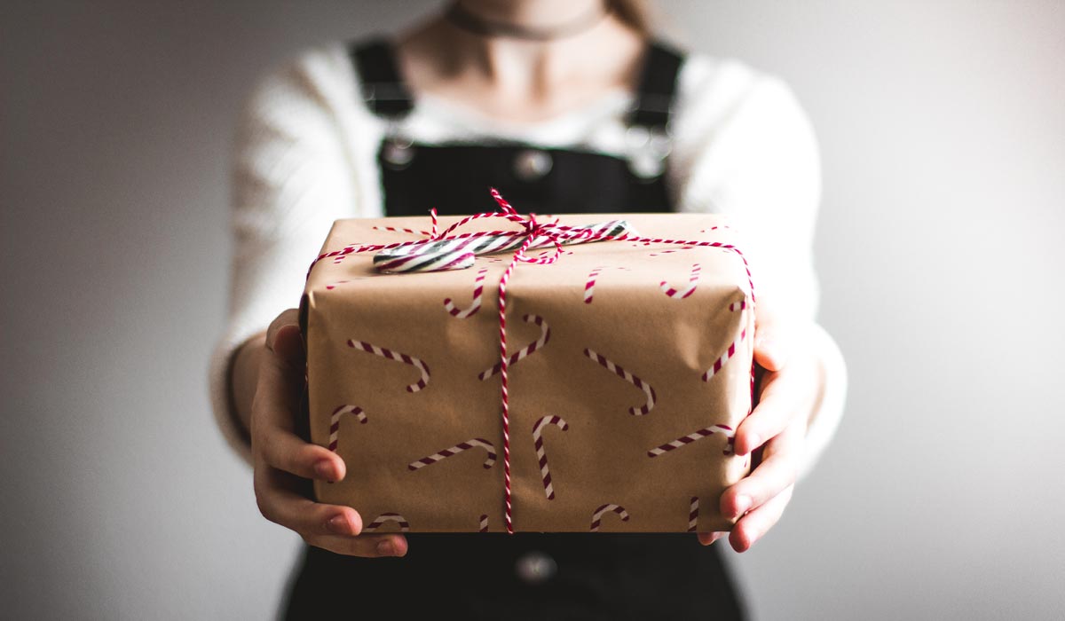 Hands holding out a wrapped Christmas present with candy cane attached