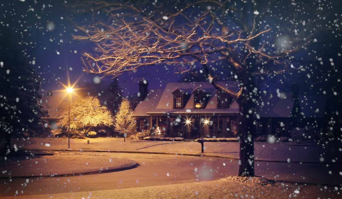 postcard like scene of snow-covered street, house and streetlight at night, with snow falling