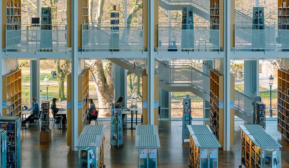 Multi-story library with book stacks, people reading at desks, all against a big glass wall.