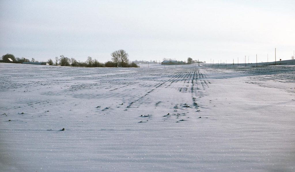 Snow covered fields with farms on the horizon on a sunny winter day in Sweden