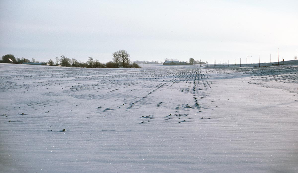 Snow covered fields with farms on the horizon on a sunny winter day in Sweden