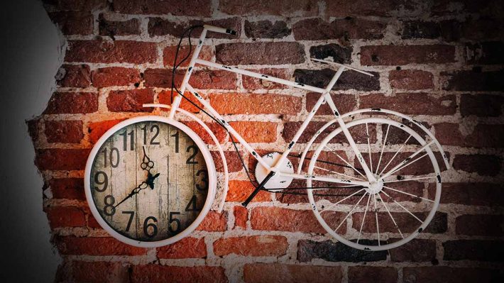 Brick wall with bicycle on it. Front wheel is a clock.
