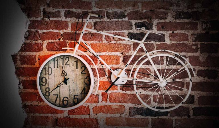 Brick wall with bicycle on it. Front wheel is a clock.