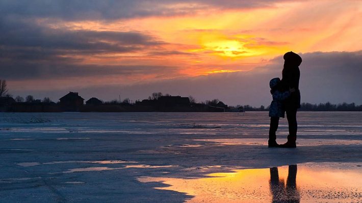 woman and child on icy field as sun rises in winter