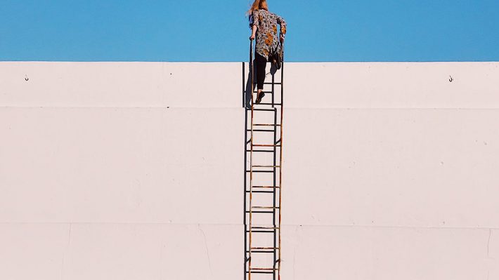 woman climbing a ladder to top of wall